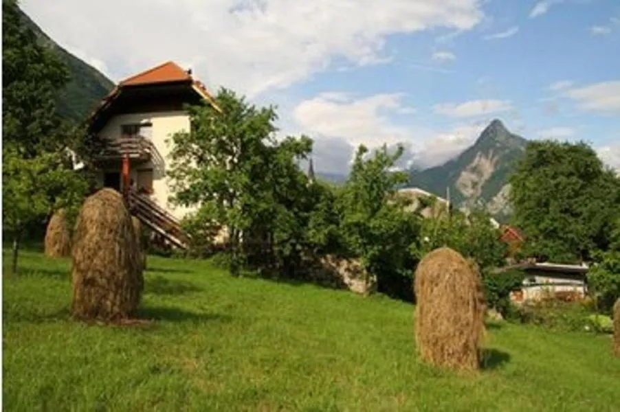 Hiša Komac nad senožetjo s kopicami sena, za njo gore nad Bovcem